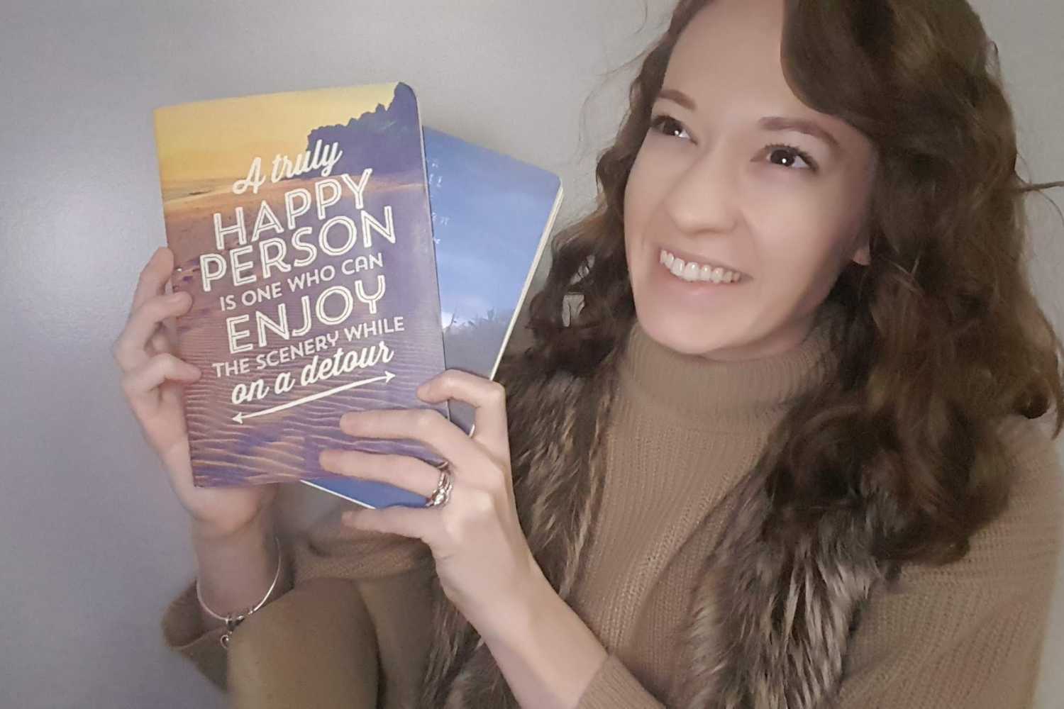 A woman holding a book that says, "A truly happy person is one who can enjoy the scenery while on a detour."