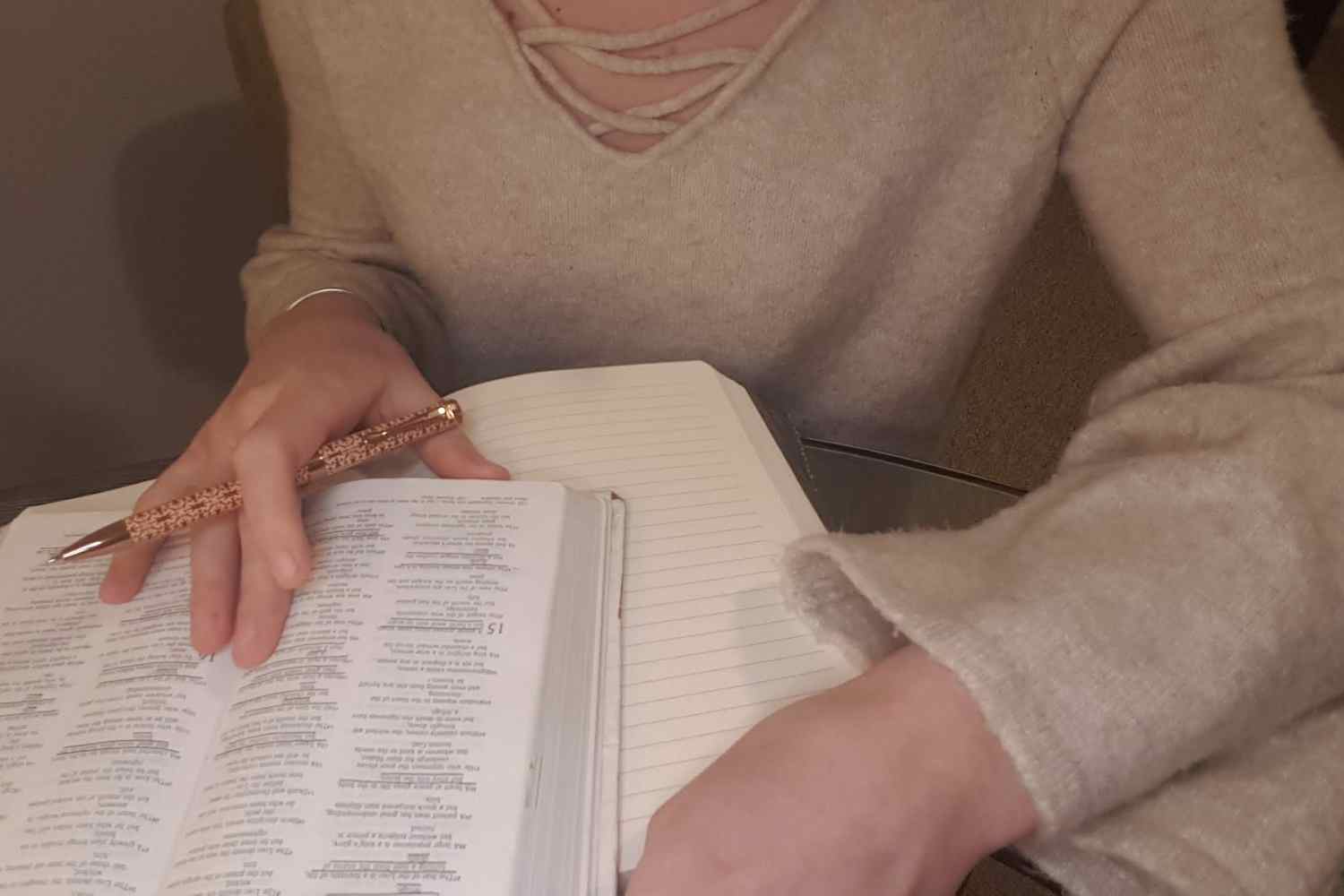 A woman in a nude sweater writing in a journal with a Bible beside her.